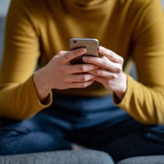 Eine junge Frau hält ein Smartphone in der Hand.