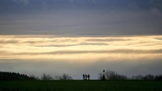 Spaziergänger sind vor einem wolkenverhangenen Himmel zu sehen. Der Deutsche Wetterdienst erwartet für Baden-Württemberg Dauerregen und Sturmböen. 