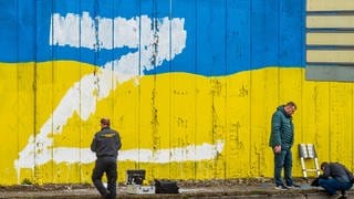 Ermittler suchen vor einer Wand, die in den Landesfarben der Ukraine angestrichen ist und auf die der Großbuchstabe Z gemalt wurde, nach Hinweisen. In Russland wird der Buchstabe Z zum Beispiel auf Autos, Häuser oder Kleidung geklebt. Sie bringen ihre Unterstützung für die russischen Streitkräfte in der Ukraine zum Ausdruck.