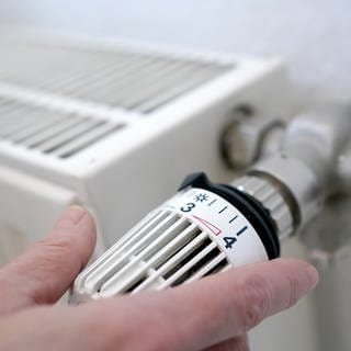 Eine Frau dreht an einem Heizungsthermostat.