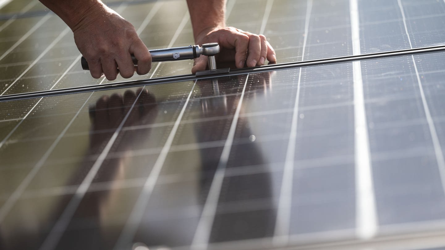 Ein Arbeiter montiert Photovoltaikmodule auf dem Dach eines Wohnhauses.