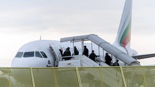 Flugzeug mit einsteigenden Passagieren, dabei erkennbar Polizei an den Türen, im Vordergrund ein gelber Zaun.