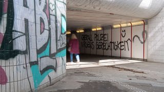 Graffitis sind in einer Unterführung in Tübingen an eine Wand gesprüht.