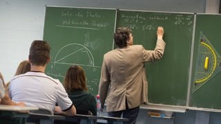 Ein Lehrer schreibt während des Matheunterrichts einer Abiturklasse an die Tafel.