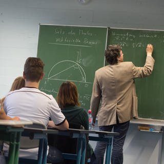 Ein Lehrer schreibt während des Matheunterrichts einer Abiturklasse an die Tafel.