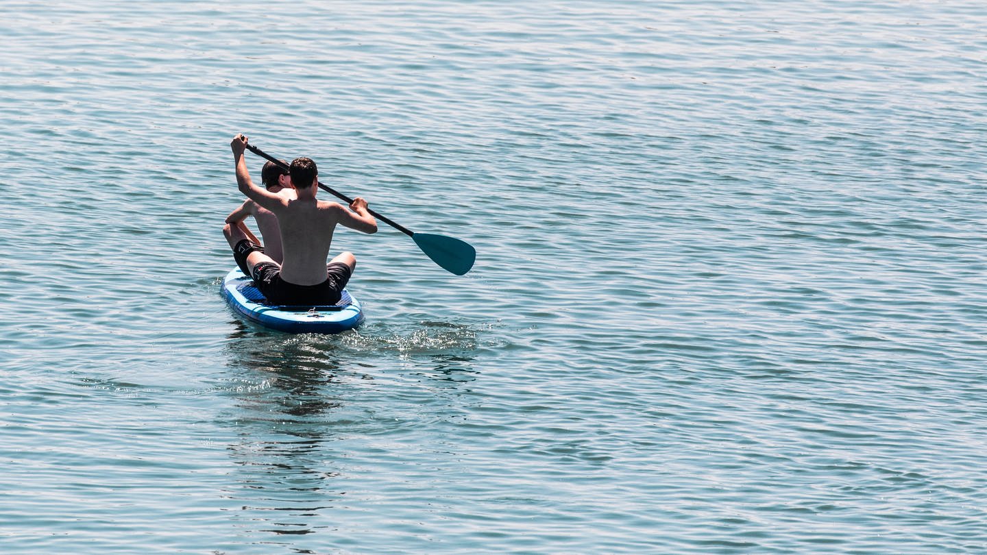 Zwei Menschen sitzen auf einem Stand-up-Paddle, einem Wassersportgerät, auf dem Epplesee in Rheinstetten.