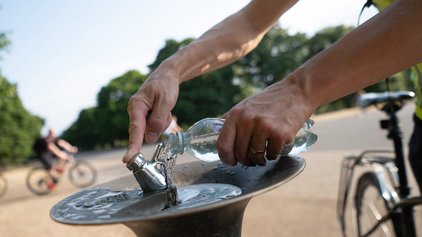 Ein Mann füllt im Park Kensington Gardens an einem Trinkbrunnen seine Wasserflasche auf.