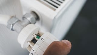 Eine männliche Hand dreht das Thermostat der Heizung auf Null. 
