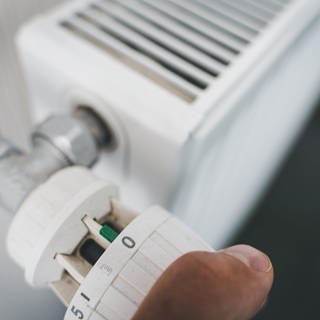 Eine männliche Hand dreht das Thermostat der Heizung auf Null. 