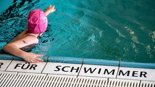 Ein Kind schwimmt in einem Schwimmbad. Auf den Fliesen steht die Aufschrift "für Schwimmer".