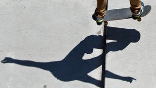 Skateboard und Beine eines Jugendlichen im Skatepark inklusive Schatten.