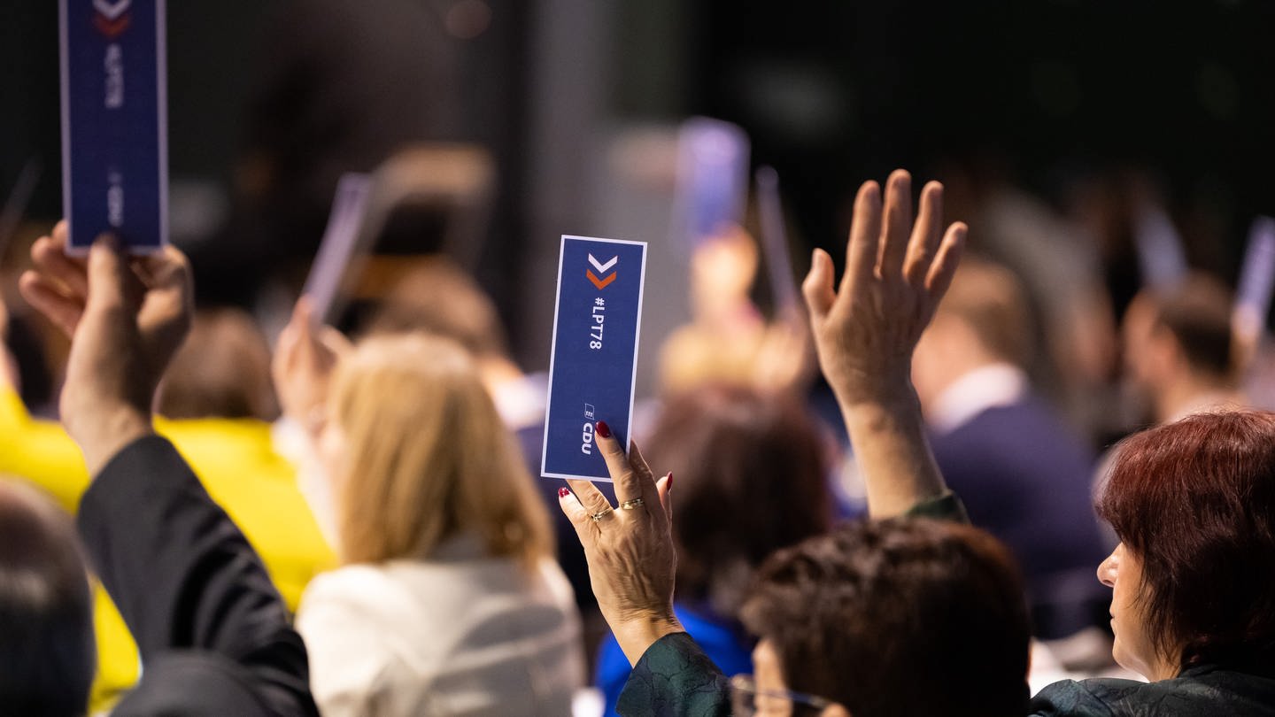 Parteimitglieder halten während den Bestimmungen der Tagesordnungspunkten beim Landesparteitag der CDU Baden-Württemberg auf dem Messegelände Stimmkarten in die Höhe.