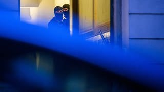 Zwei Maskierte Polizisten durchsuchen ein Gebäude. 