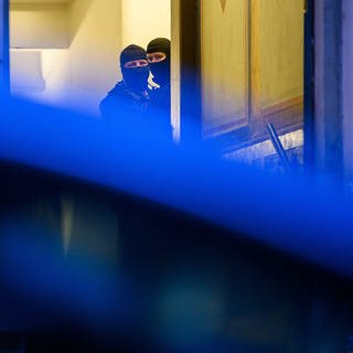 Zwei Maskierte Polizisten durchsuchen ein Gebäude. 