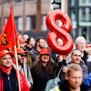 Eine Teilnehmerin hält in der Innenstadt bei einer Aktion der Gewerkschaft IG Metall im Tarifkonflikt der Metall- und Elektroindustrie eine rote Acht in die Höhe.