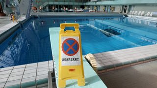 Ein "Gesperrt"-Schld steht vor einem Schwimmbecken mit Wasser, aber ohne Schwimmer