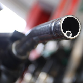 Eine Frau hält an einer Tankstelle vor einer Zapfsäule eine Zapfpistole.