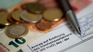 Antrag auf Eröffnung des Insolvenzverfahrens liegt neben Münzen und einem 10-Euro-Schein auf dem Tisch (Symbolbild)