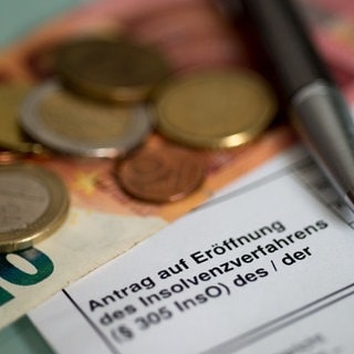 Antrag auf Eröffnung des Insolvenzverfahrens liegt neben Münzen und einem 10-Euro-Schein auf dem Tisch (Symbolbild)