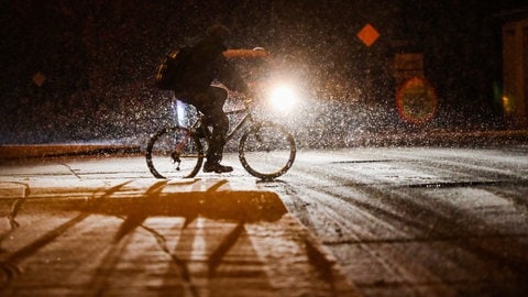 Ein Radfahrer fährt bei Schneefall auf einer mit Schnee bedeckten Straße. 