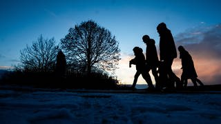 Spaziergänger gehen zur blauen Stunde über einen Feldweg. In vielen Teilen von Baden-Württemberg gab es den ersten Schnee, in höheren Lagen blieb dieser auch liegen.