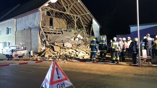 Feuerwehrleute stehen vor einer eingestürzten Hauswand.