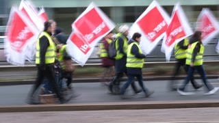 Teilnehmer einer Demonstration der Gewerkschaft Verdi laufen mit Fahnen der Gewerkschaft eine Straße entlang.