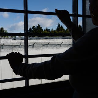Ein Mann steht in seiner Gefängniszelle und blickt auf den Hof