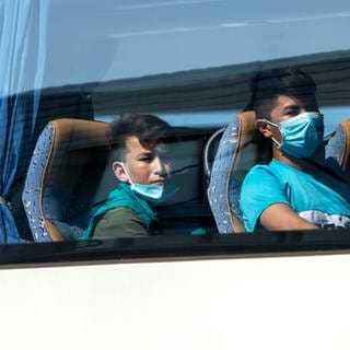 Junge Flüchtlinge, teilweise mit Mundschutz, sitzen in einem Bus