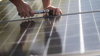 Ein Arbeiter montiert Photovoltaikmodule auf dem Dach eines Wohnhauses. 