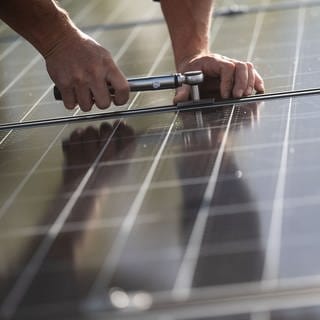 Ein Arbeiter montiert Photovoltaikmodule auf dem Dach eines Wohnhauses. 