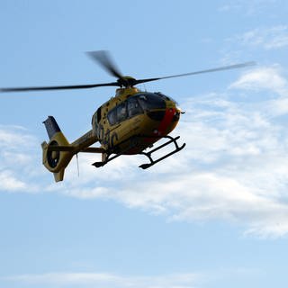 Ein Hubschrauber der ADAC Luftrettung fliegt über einer Unfallstelle von einem verunglückten Bus.