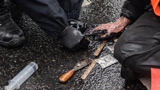 Ein Polizeibeamter versucht die festgeklebte Hand eines Demonstranten der Umweltschutzgruppe "Letzte Generation" vom Asphalt zu lösen. 