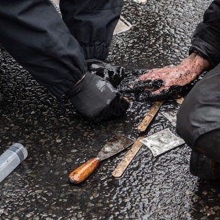 Ein Polizeibeamter versucht die festgeklebte Hand eines Demonstranten der Umweltschutzgruppe "Letzte Generation" vom Asphalt zu lösen. 