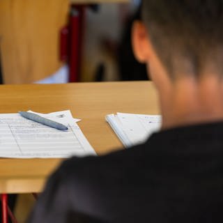 Ein Stift und Arbeitsblätter liegen vor einem Schüler.
