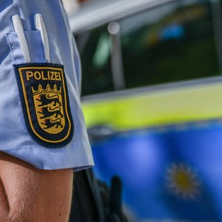 Ein Beamter der Polizei Baden-Württemberg vor einem Polizeiauto