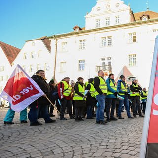 Mitglieder der der Gewerkschaft Verdi stehen bei einer Kundgebung mit Fahnen auf dem Marktplatz in Rottenburg.