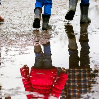 Eine Frau und ihre Kinder gehen auf einem Weg auf dem sich Regenpfützen gebildet haben.