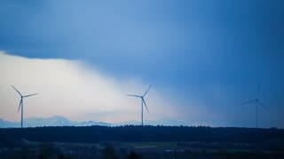 Hinter drei Windrädern ziehen Regenwolken auf.