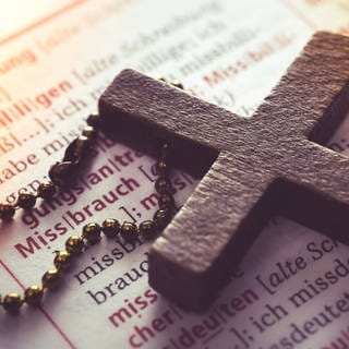 Symbolbild für Missbrauch in der katholischen Kirche: Ein Kreuz liegt auf einem Wörterbuch (Eintrag Missbrauch) 