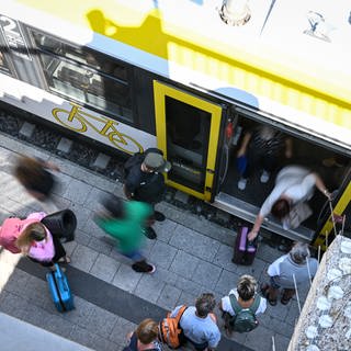 Zugreisende stehen an einem Bahnsteig in Überlingen (Bodenseekreis) bereit, um in einen Zug einzusteigen. 