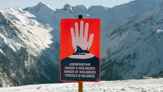 Österreich, Wildkogel: Ein Schild warnt im Skigebiet auf dem Wildkogel bei Neukirchen im Bundesland Salzburg in den Alpen in Österreich vor Lawinengefahr. Im Hintergrund das Massiv des Großvenedigers. 