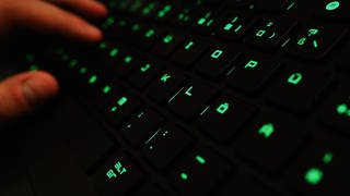 Ein Mann tippt auf einer beleuchteten Tastatur an einem Laptop. Symbolbild zu Hackerangriff auf IT-Dienstleister für Krankenkassen.