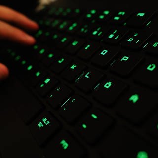 Ein Mann tippt auf einer beleuchteten Tastatur an einem Laptop. Symbolbild zu Hackerangriff auf IT-Dienstleister für Krankenkassen.
