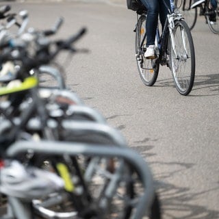 Eine Radfahrerin fährt in der Innenstadt an geparkten Fahrrädern vorbei. 