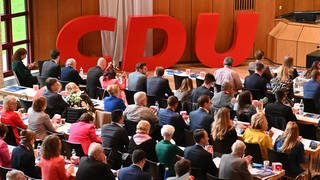 Die CDU-Vertreterinnen und -Vertreter hören vor einem CDU-Logo in der Filderhalle einer Rede auf der Landesvertreterversammlung zu.