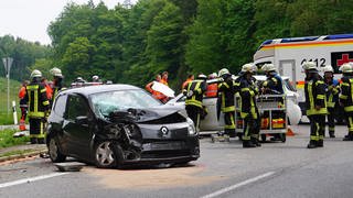 Rettungskräfte stehen am Ort eines Unfalls neben den beschädigten Fahrzeugen. Bei dem Autounfall auf einer Bundesstraße bei Grünkraut im Keis Ravensburg sind am Samstag elf Menschen verletzt worden, darunter auch drei Kinder.