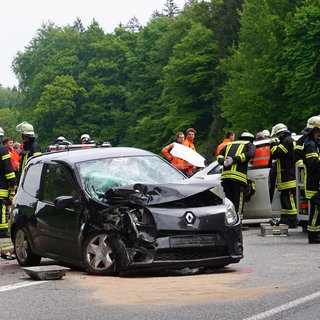 Rettungskräfte stehen am Ort eines Unfalls neben den beschädigten Fahrzeugen. Bei dem Autounfall auf einer Bundesstraße bei Grünkraut im Keis Ravensburg sind am Samstag elf Menschen verletzt worden, darunter auch drei Kinder.