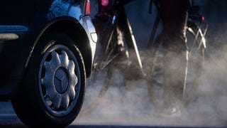 Ein Radfahrer steht neben einem Auto von Mercedes mit Dieselantrieb, dessen Abgase in der kalten Morgenluft sichtbar werden (Symbolbild). 