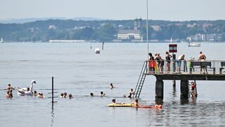 Badegäste schwimmen im Bodensee oder stehen auf dem Steg des Frei- und Strandbads in Langenargen.